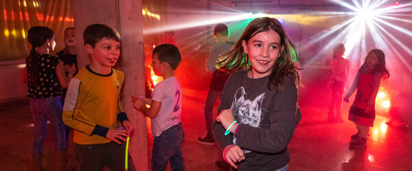 Teilnehmende der Kinderdisco tanzen, und Lichteffekte strahlen sternförmig