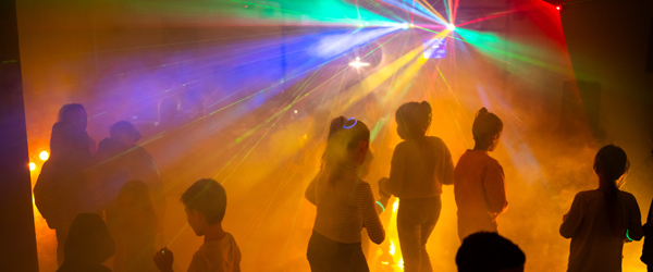 Teilnehmende der Kinderdisco tanzen und Lichteffekte leuchten farbig