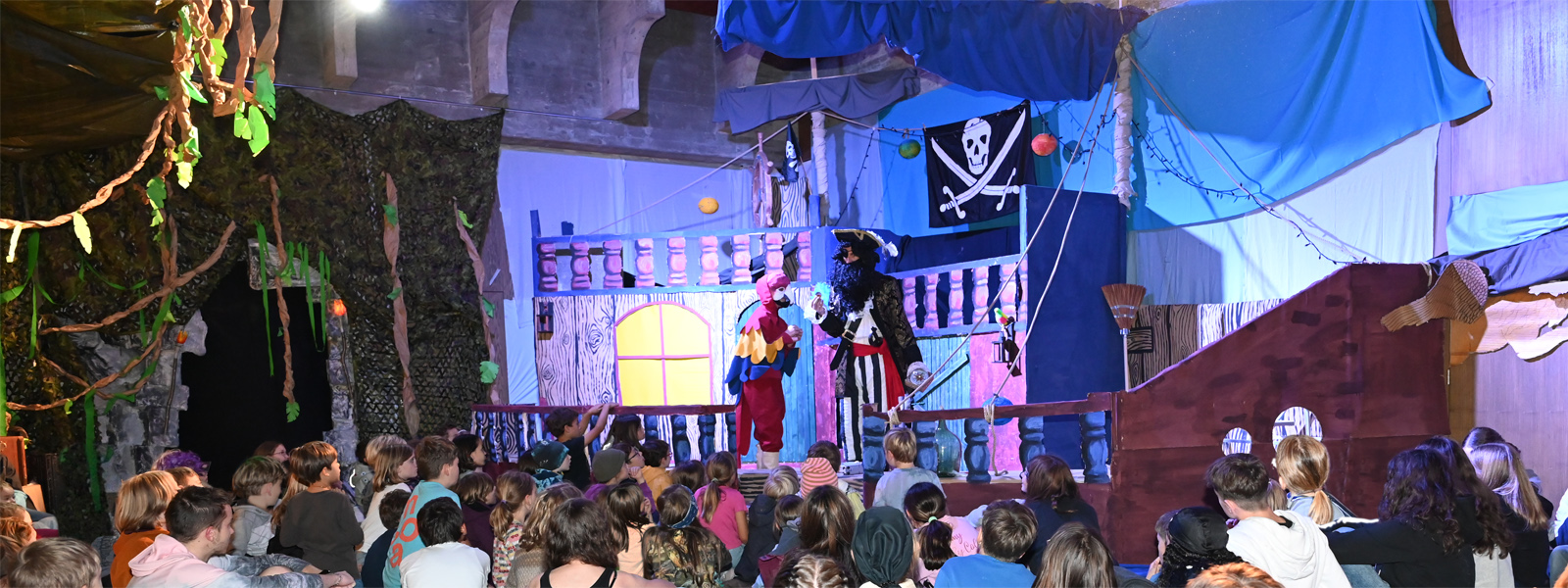 Kinder schauen ein Theater mit einem Piraten und einem Papagei auf einem Segelschiff